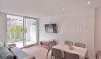 Helles Wohnzimmer mit Essbereich, grauem Sofa, TV und Balkon mit Palmenblick in Palmanova-Apartment