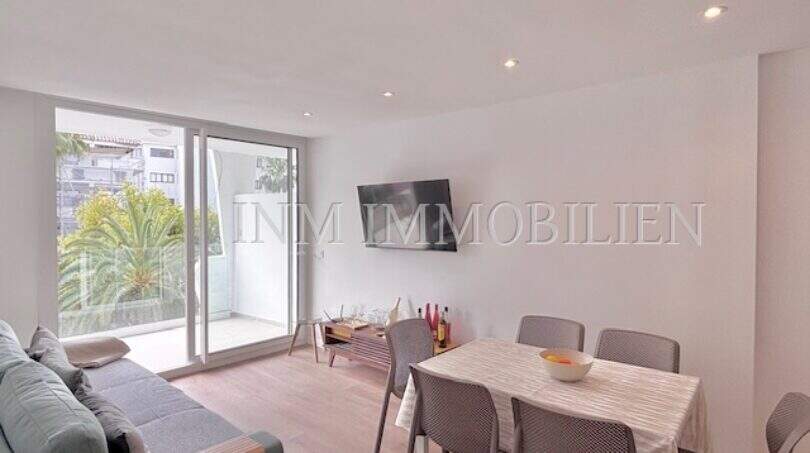 Helles Wohnzimmer mit Essbereich, grauem Sofa, TV und Balkon mit Palmenblick in Palmanova-Apartment