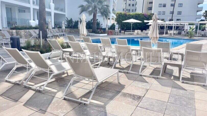 Poolbereich mit weißen Liegestühlen, Sonnenschirmen und modernen Apartments in Palmanova