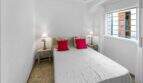 Luminoso dormitorio con cama doble, cojines rojos, cabecero de madera y ventana con vista al exterior en la casa de ciudad Felanitx