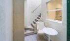Pequeño patio interior con escalera de hormigón, silla y mesa blancas así como vista de ventana al interior de la casa de ciudad en Felanitx.