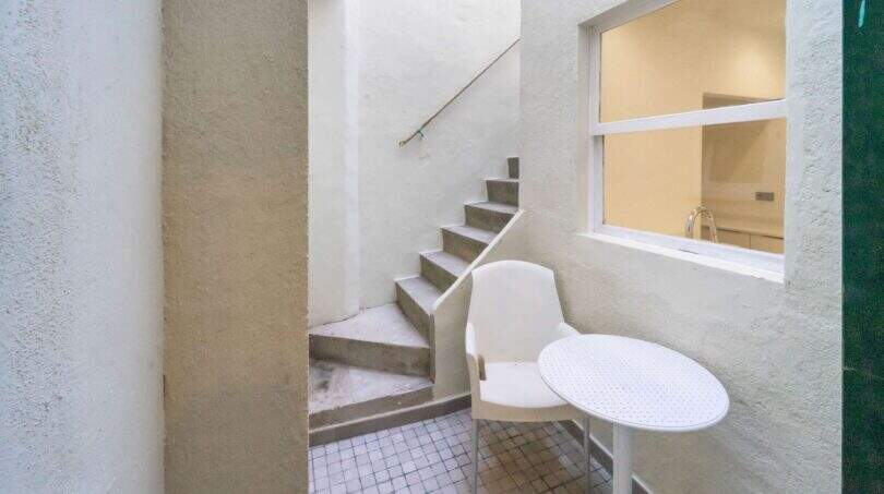 Pequeño patio interior con escalera de hormigón, silla y mesa blancas así como vista de ventana al interior de la casa de ciudad en Felanitx.