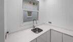 Pequeña cocina blanca con fregadero de acero inoxidable, armarios modernos inferiores y ventana en la casa de ciudad Felanitx