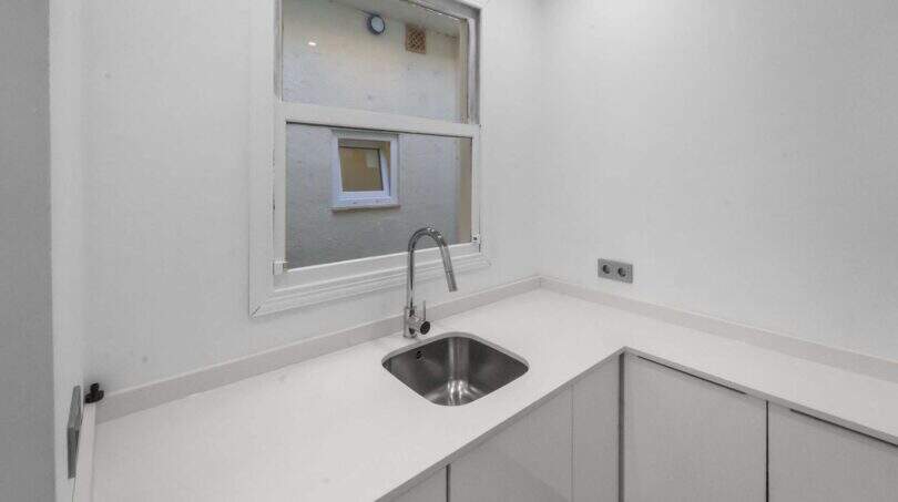 Pequeña cocina blanca con fregadero de acero inoxidable, armarios modernos inferiores y ventana en la casa de ciudad Felanitx