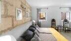 Dormitorio con pared de piedra natural, cama doble gris, corredor amarillo y sillas antiguas de madera en Felanitx