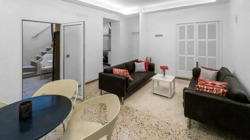 Luminosa sala de estar con sofás marrón oscuro, cojines de acento rojos, mesa de centro blanca y mesa de comedor moderna en Felanitx