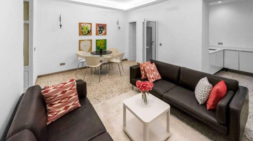 Luminosa sala de estar con dos sofás de cuero oscuro, mesa de centro blanca e imágenes de arte pop en la pared en la casa de ciudad Felanitx