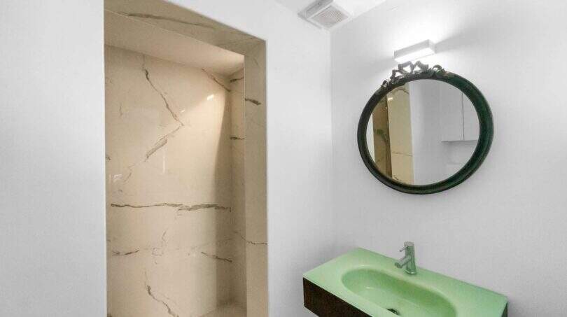 Moderno baño con lavamanos verde, espejo redondo y ducha de mármol en la casa de ciudad Felanitx