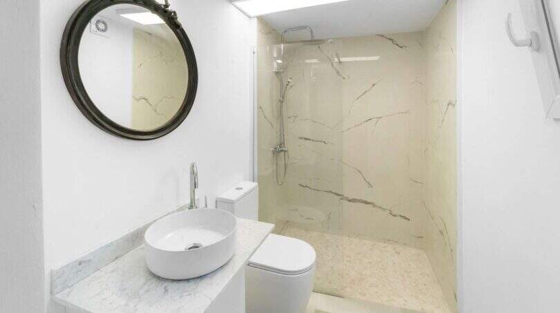 Moderno baño con ducha de mármol, lavamanos tipo recipiente y espejo vintage redondo en la casa de ciudad Felanitx
