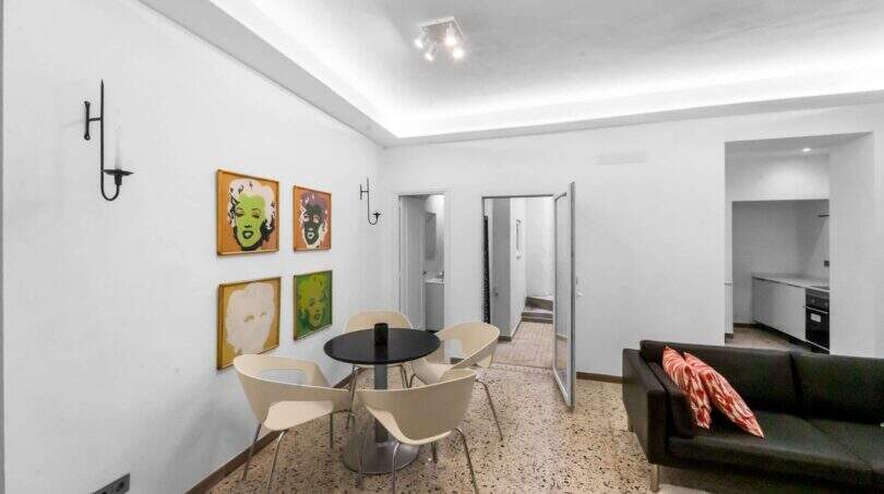Luminosa sala de estar con mesa de comedor negra, sillas modernas e imágenes de arte pop en la pared en la casa de ciudad Felanitx