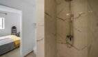 Elegante baño de mármol con ducha de lluvia, vista al dormitorio con acento amarillo, casa de ciudad Felanitx