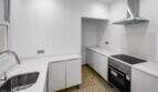 Moderna cocina blanca con horno empotrado, placa de inducción, campana extractora de acero inoxidable y suelo de terrazo en la casa de ciudad Felanitx