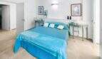 Luminoso dormitorio con cama doble turquesa, mesillas de noche verdes y paredes blancas en la casa de ciudad Felanitx