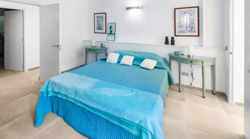 Luminoso dormitorio con cama doble turquesa, mesillas de noche verdes y paredes blancas en la casa de ciudad Felanitx