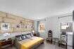 Dormitorio con pared de piedra natural, cama doble con colcha amarilla y sillas de madera antiguas en la casa urbana Felanitx