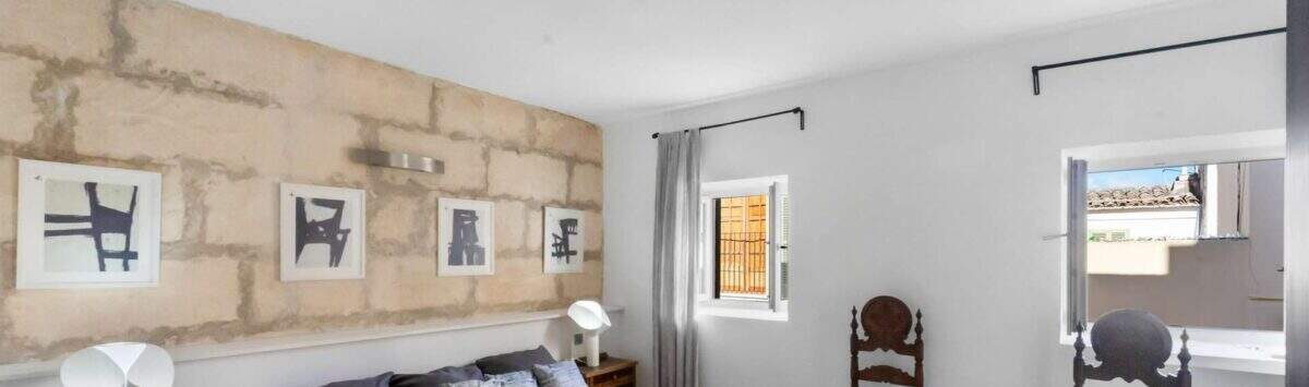 Dormitorio con pared de piedra natural, cama doble con colcha amarilla y sillas de madera antiguas en la casa urbana Felanitx