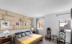 Schlafzimmer mit Natursteinwand, Doppelbett mit gelber Decke und antiken Holzstühlen im Stadthaus Felanitx