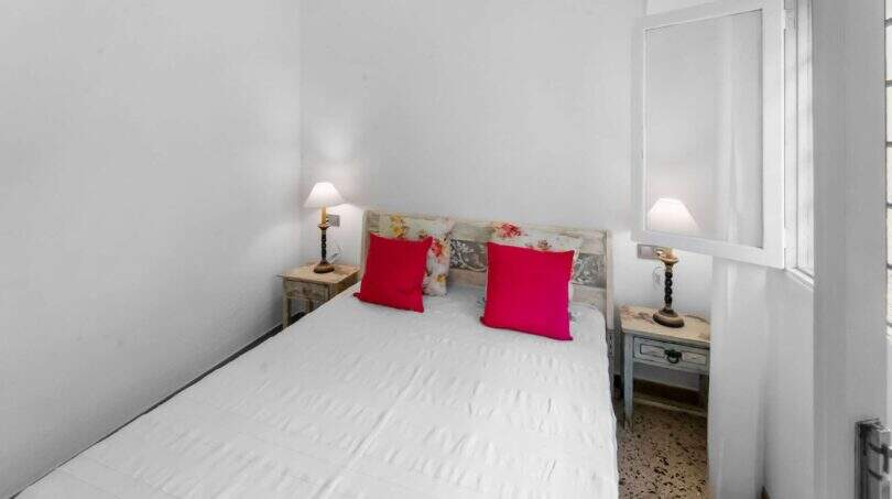 Luminoso dormitorio con cama doble, cojines rojos y mesillas de noche rústicas en la casa de ciudad Felanitx
