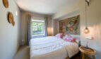 Helles Schlafzimmer der Finca in Esporles mit Doppelbett, buntem Wandteppich und rustikalem Holzbeistelltisch.