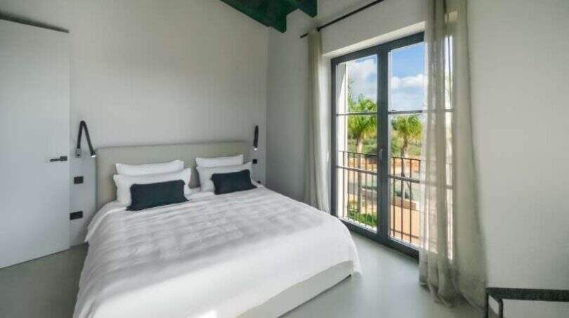 Helles Schlafzimmer der Finca Portocolom mit Doppelbett, schwarzen Akzenten und Balkon mit Palmenblick.