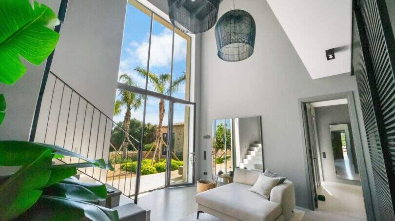 Helles Wohnzimmer der Finca Portocolom mit Doppeldecke, Designerlampen und Panoramablick auf Palmen