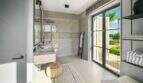 Modernes Badezimmer der Finca bei Portocolom mit Walk-in-Dusche, Naturstein-Waschtisch und Ausblick ins Grüne.