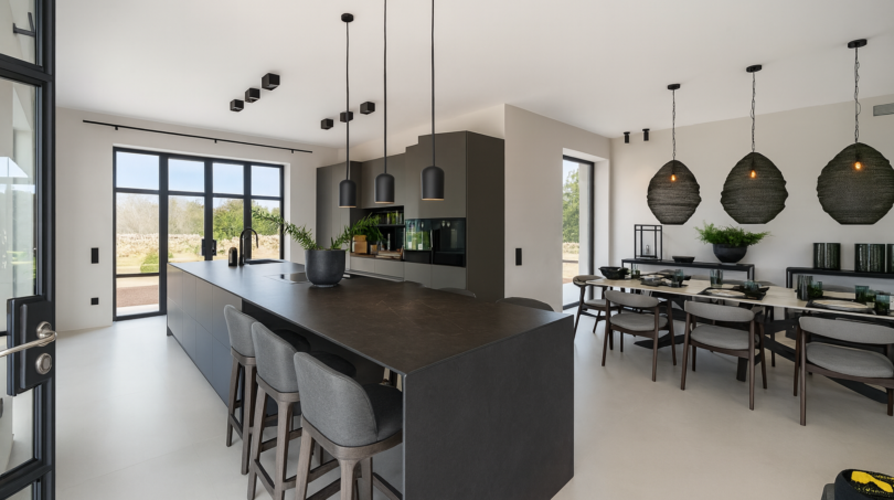 Moderne Küche mit dunkler Kochinsel, Barstühlen und elegantem Essbereich der Finca bei Portocolom