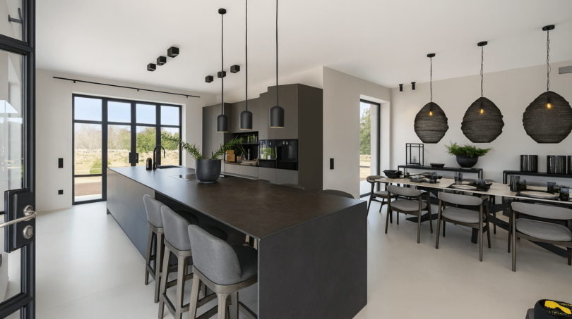 Offene Küche mit dunkler Kochinsel, Barhockern und modernem Essbereich der Finca nahe Cala Sa Nau in Portocolom