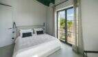 Helles Schlafzimmer der Finca bei Portocolom mit Doppelbett, grünen Holzbalken und Balkon mit Meerblick.
