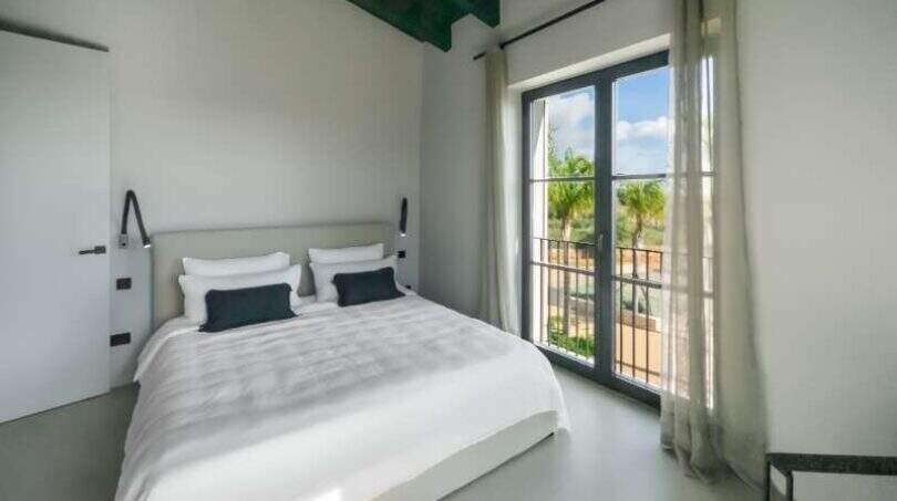 Helles Schlafzimmer der Finca bei Portocolom mit Doppelbett, grünen Holzbalken und Balkon mit Meerblick.