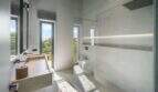 Modernes Badezimmer der Finca Portocolom mit Glasdusche, Naturstein-Waschtisch und Panoramafenstern mit Gartenblick