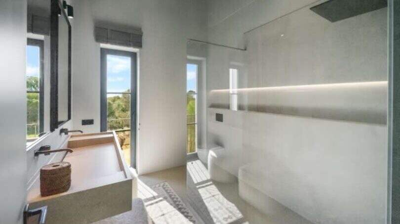 Modernes Badezimmer der Finca Portocolom mit Glasdusche, Naturstein-Waschtisch und Panoramafenstern mit Gartenblick