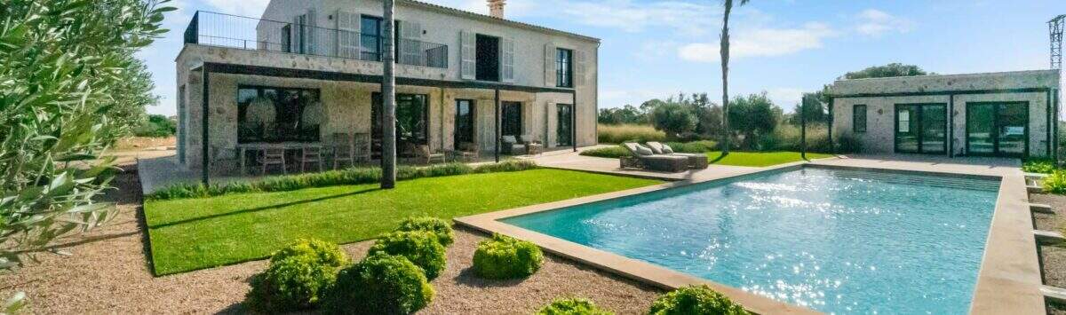 Finca Portocolom: piscina de estilo mediterráneo con zona ajardinada, palmeras y una villa de piedra natural en una ubicación de ensueño