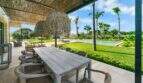 Überdachte Außenterrasse der Finca Portocolom mit Holztisch, Rattanstühlen, Palmen und Pool im Hintergrund