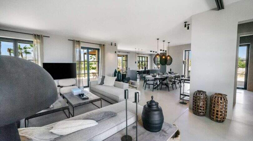 Heller Wohnbereich der Finca Portocolom mit modernem Sofa, Esstisch und Meerblick-Fenstern zu Palmen.