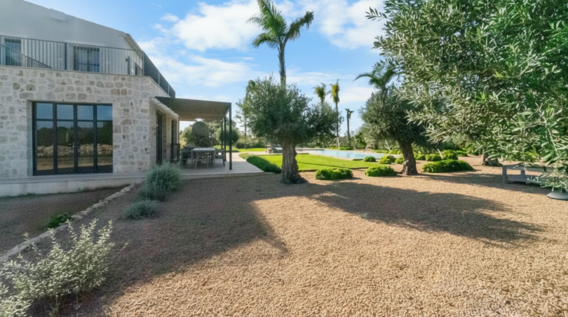 Finca Portocolom: Natursteinvilla mit Kiesweg, Olivenbäumen, Palmen und Pool im mediterranen Garten.