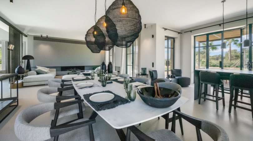 Elegantes Esszimmer der Finca Portocolom mit langen Marmortisch, Designer-Hängeleuchten und Blick ins Grüne