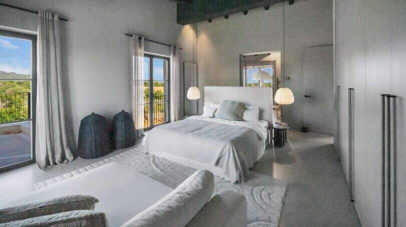 Helles Schlafzimmer der Finca Portocolom mit weißem Doppelbett, Pendelleuchten und Balkon mit Landschaftsblick.
