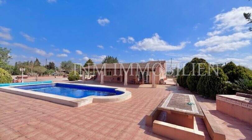Weitläufige Terrasse mit Pool und Springbrunnen der Finca in Llucmajor unter blauem Himmel