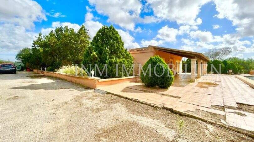 Außenansicht Finca Llucmajor: Bungalow mit überdachter Terrasse, Säulengang, Zypressen und großem Vorplatz.