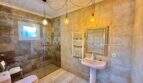 Badezimmer der Finca in Llucmajor mit Natursteinoptik, Glasdusche, Hängelampen und goldenem Spiegel.