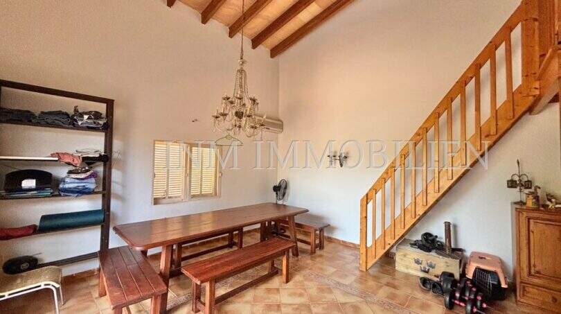 Rustikales Esszimmer der Finca in Llucmajor mit Holzbalkendecke, Esstisch und Holztreppe ins Obergeschoss.