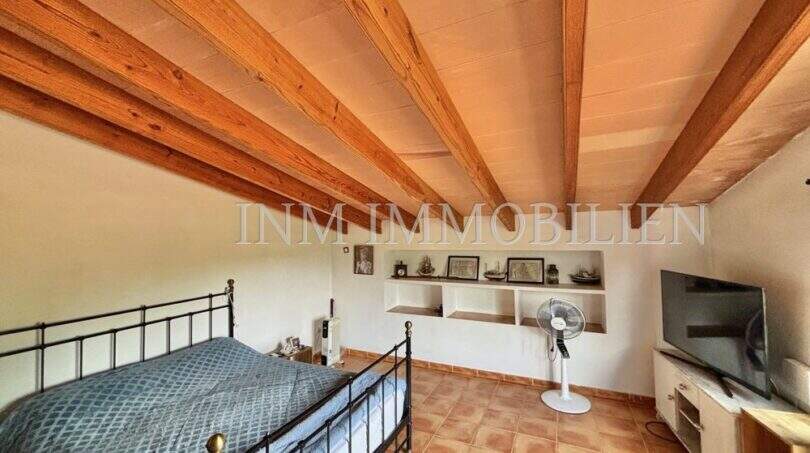 Schlafzimmer mit Holzbalkendecke, Doppelbett, Wandregalen und Terrakottaboden in Finca Llucmajor