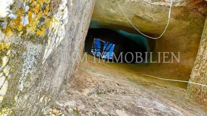 Blick in einen tiefen Felsenschacht mit Rostgitter der Finca in Llucmajor, unten sichtbares Wasser