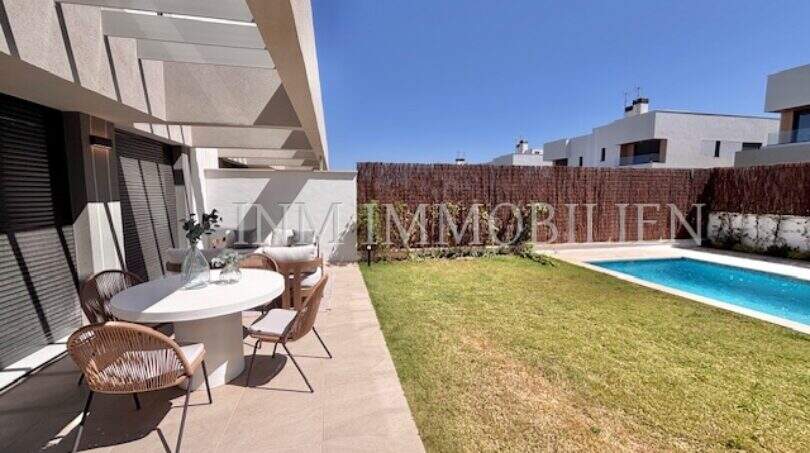 Terraza moderna con mesa de comedor, jardín bien cuidado y piscina privada de una casa de nueva construcción en Puig de Ros