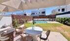 Terraza cubierta con mesa de comedor, lounge y jardín bien cuidado con piscina de una casa de nueva construcción en Puig de Ros