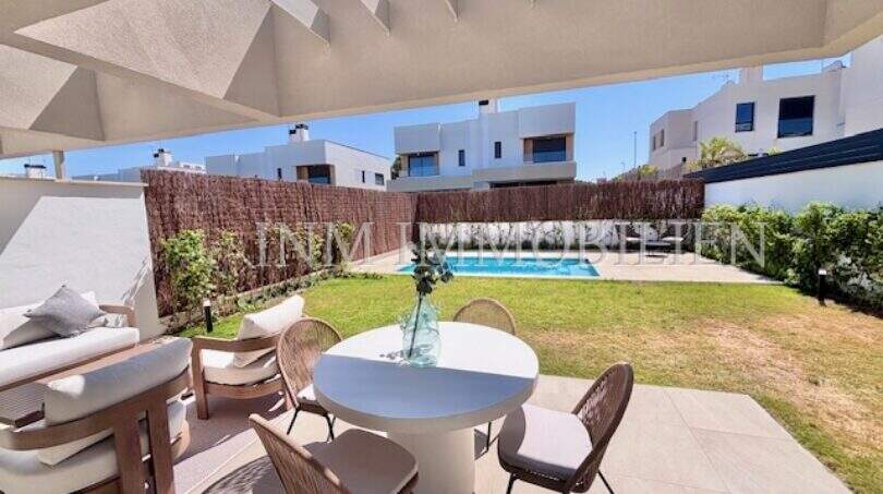 Terraza cubierta con mesa de comedor, lounge y jardín bien cuidado con piscina de una casa de nueva construcción en Puig de Ros
