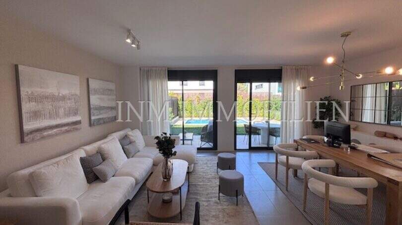 Luminosa sala de estar con sofá blanco, moderna mesa de comedor y frente de cristal con vista a la piscina privada en Puig de Ros