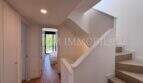Pasillo luminoso con suelo de madera, moderno tramo de escaleras y vista al dormitorio en la casa de nueva construcción Puig de Ros