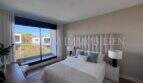 Dormitorio luminoso con cabecero acolchado, ropa de cama blanca y gran ventanal panorámico con balcón en la nueva construcción Puig de Ros